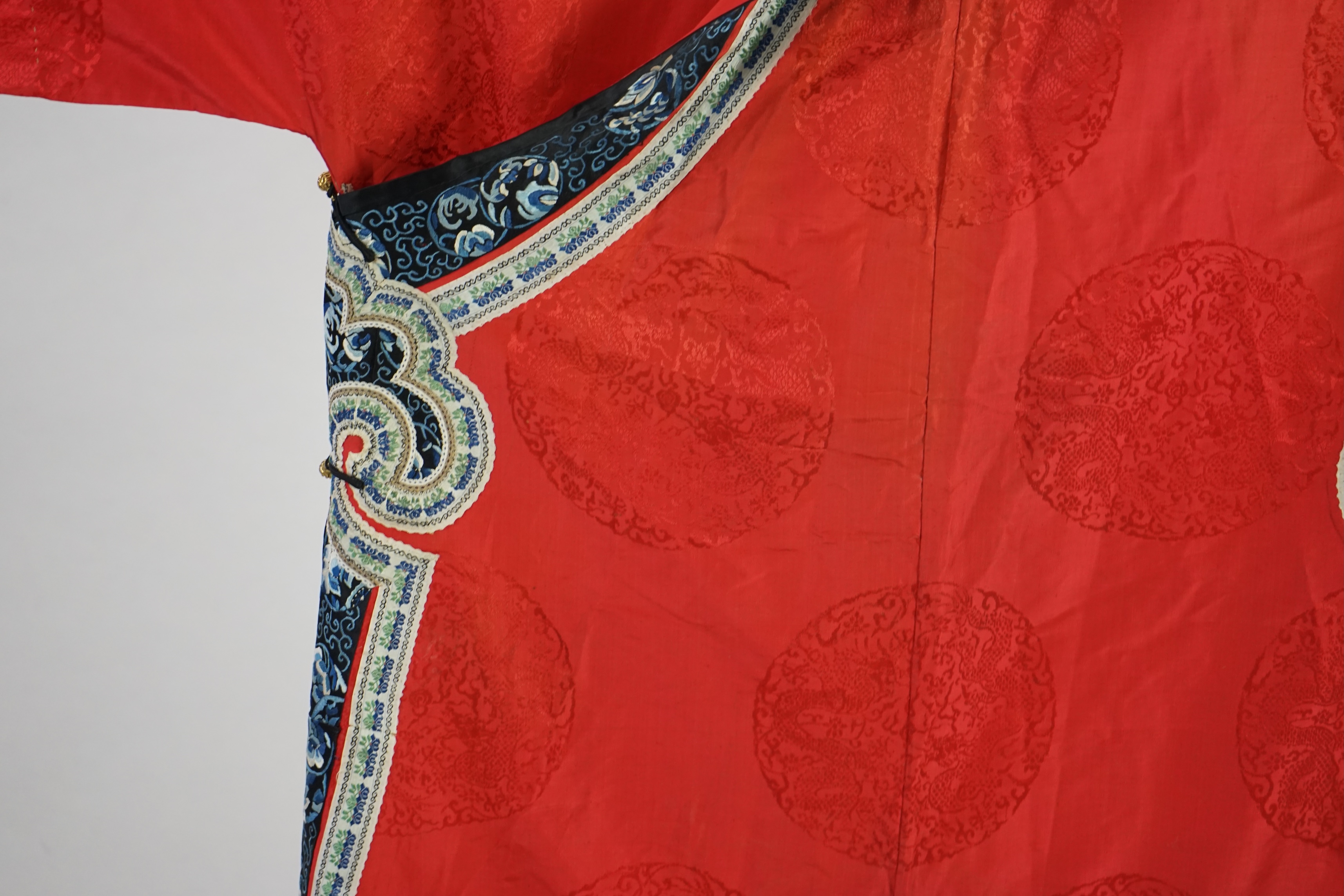 A late 19th century Chinese Manchu ladies red silk damask robe, with black and blue silk embroidered borders, ornately edged cream floral silk braiding, length from neck (back) to bottom edge 132cm long. Condition - stai